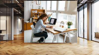 Young woman sitting at desk working on laptop
 Wall mural